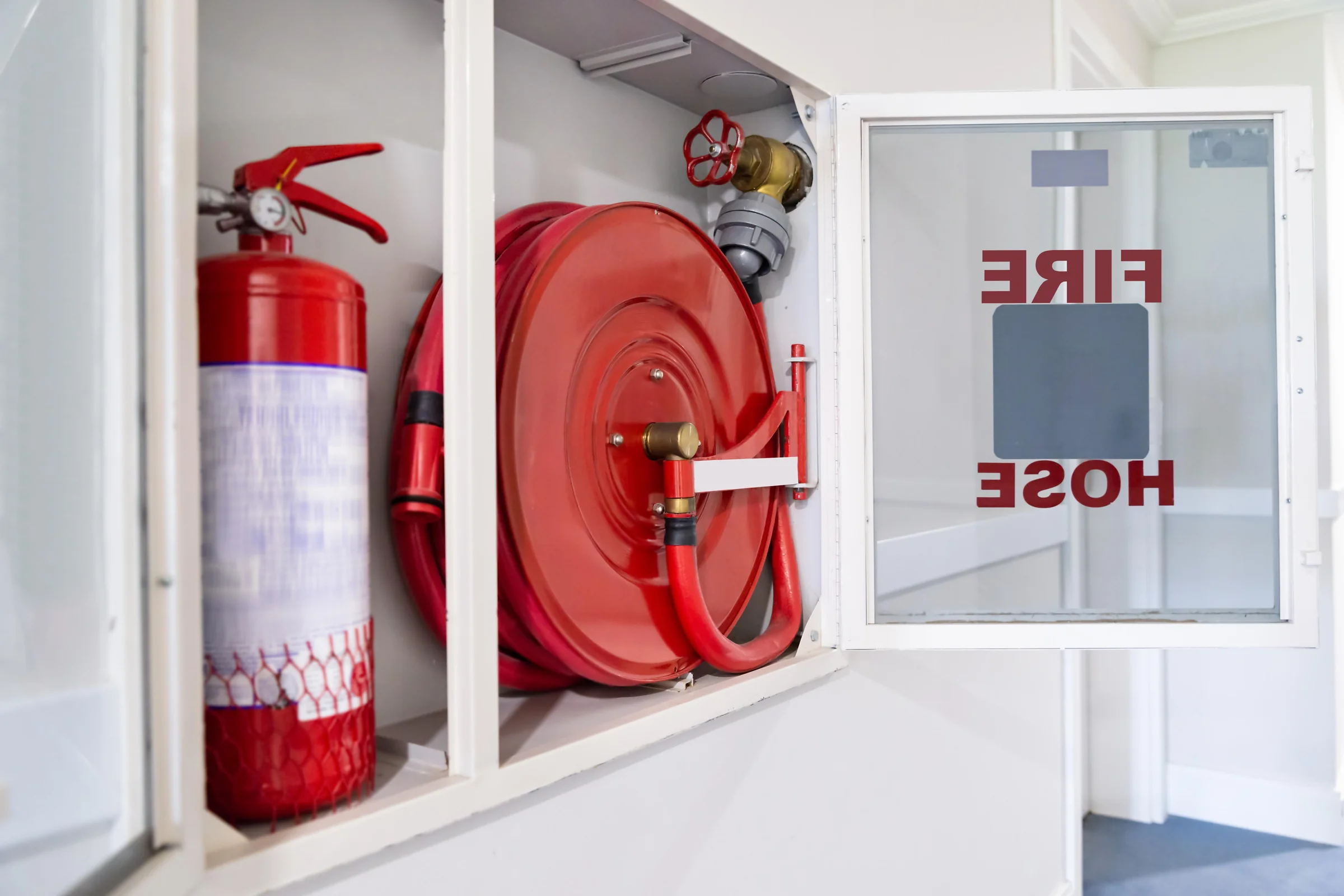 Armoire incendie ouverte : robinet d’incendie armé enroulé sur son dévidoir, à côté d’un extincteur